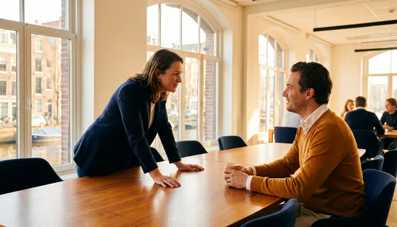 B2B accountmanager luistert aandachtig naar klant aan conferentietafel in modern Amsterdams kantoor met natuurlijk licht.