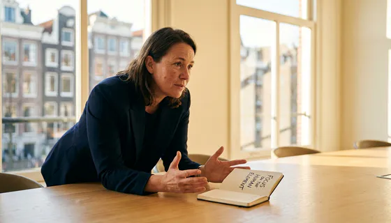 B2B-professional leunt aandachtig voorover aan een minimalistische vergadertafel met open notitieboek in warm Amsterdams kantoorlicht.