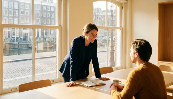 Professional luistert aandachtig naar cliënt aan minimalistische kantoortafel in Amsterdam, met notitieboek en koffiekopje in warm natuurlijk licht.